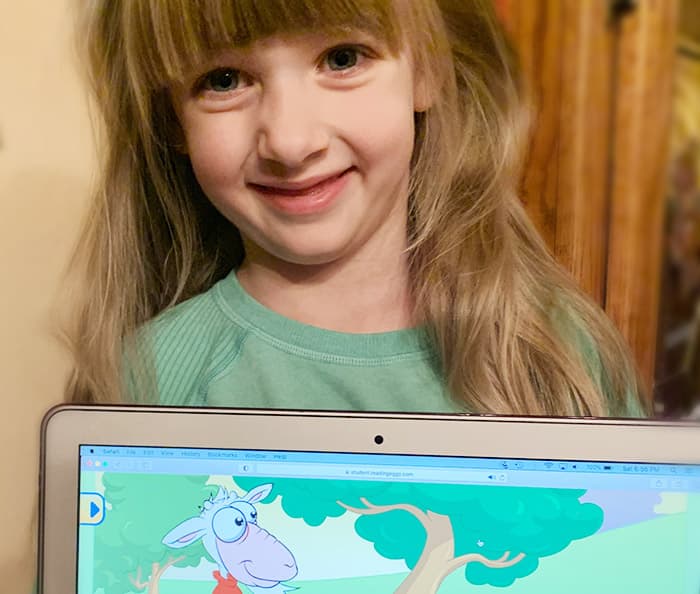 Smiling five year old girl with ABC Reading Eggs online program on laptop.