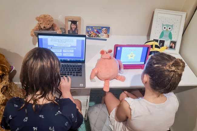 Six-year-old girl and four-year-old-girl work on their ABC Reading Eggs lessons on iPad and laptop.