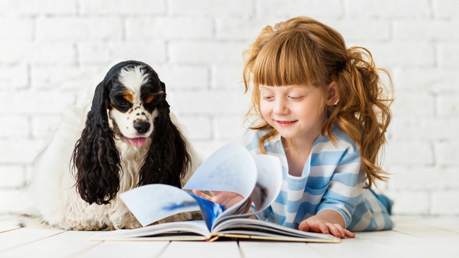 Four-year-old girl learning how to read with her puppy