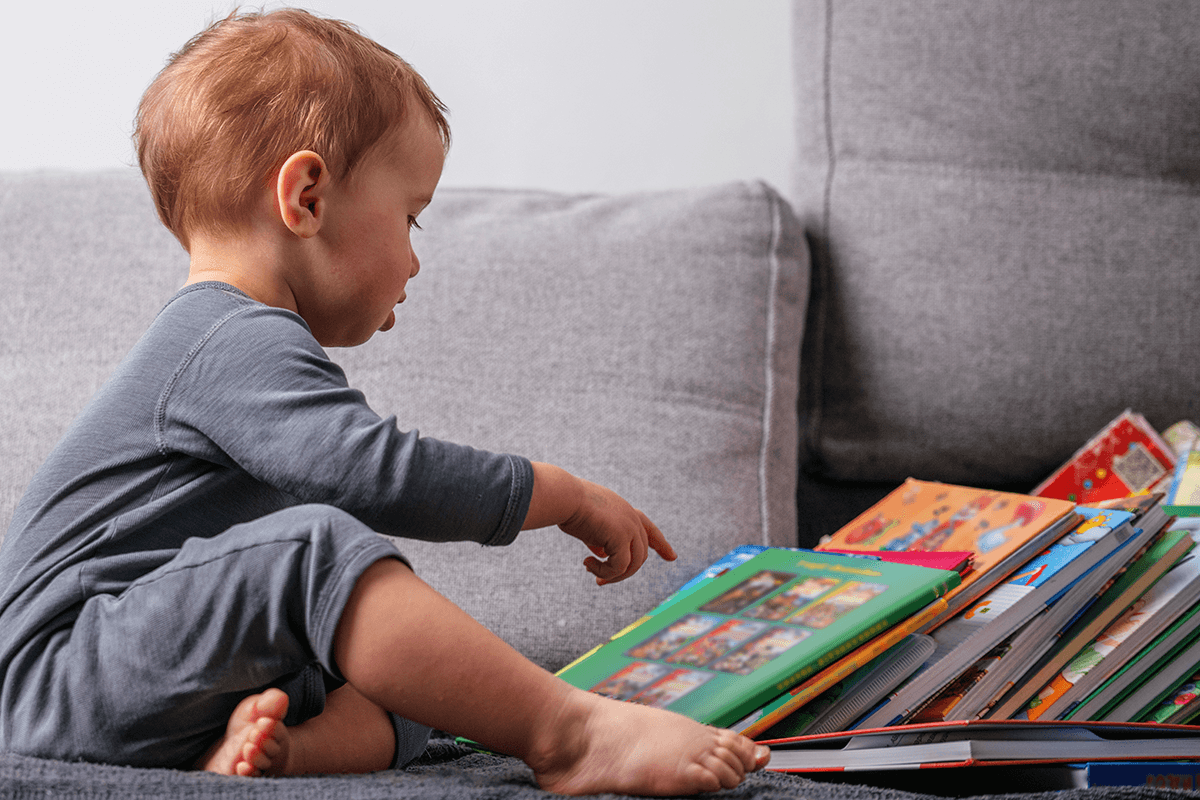 toddler pointing at a pile of books – recognising the covers of books they love is a reading milestone for toddlers